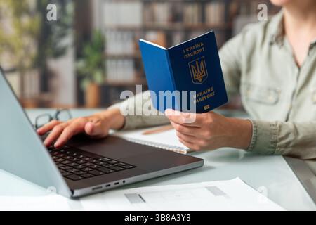 Nahaufnahme weiblicher Hände mit ukrainischem Pass, der Daten über Laptop eingibt . Ukrainisches biometrisches internationales Passortkonzept Stockfoto