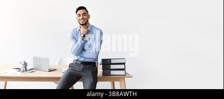 Lächelnder, gutaussehender, erfolgreicher, selbstbewusster junger arabischer Geschäftsmann denkt, er sitzt im Büro Stockfoto