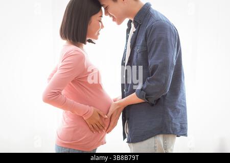 Liebevolle asiatische Mann berühren schwangere Frau Bauch zu Hause stehend Stockfoto