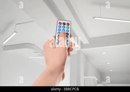 Frau, die die Beleuchtung im Zimmer mit Fernbedienung steuert, Nahaufnahme Stockfoto