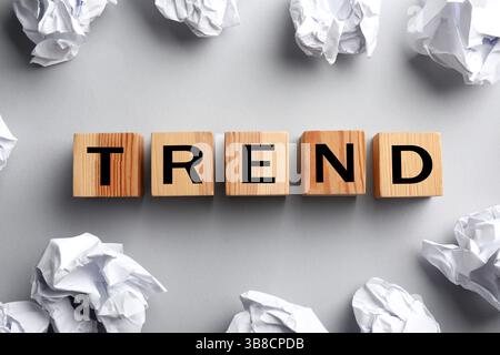 Word Trend aus Holzwürfeln mit Buchstaben und zerknitterten Papierkugeln auf hellgrauem Hintergrund, Draufsicht Stockfoto
