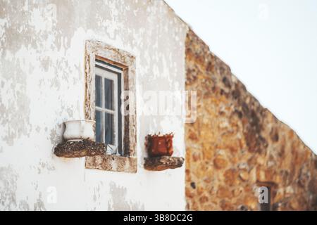 Nahaufnahme einer verwitterten rustikalen Hausfassade mit einer abgebrochenen weißen Wand, einem Vintage-Fenster, das in Stein eingerahmt ist, und zwei traditionellen Keramiktöpfen Stockfoto