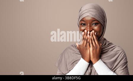 Lachen. Positive Schwarze Muslimische Frau In Hijab Bedeckt Den Mund Mit Händen Stockfoto