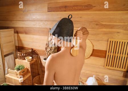 Junger Mann massiert sich in der Sauna den Rücken mit einer Bürste Stockfoto