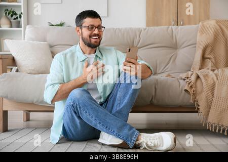 Überraschter junger Mann, der zu Hause ein Handy benutzt Stockfoto