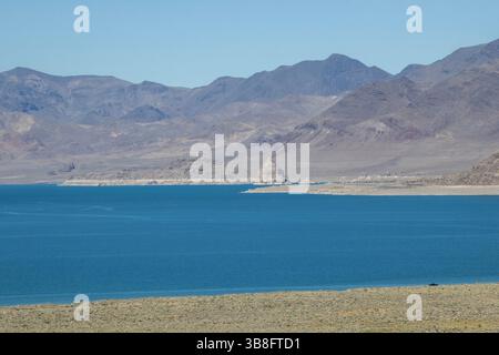 Das lebhafte blaue Wasser erstreckt sich über das Seeufer, umgeben von zerklüfteten Bergen im Hintergrund. Der klare Himmel verstärkt die ruhige und einladende Atmosphäre Stockfoto