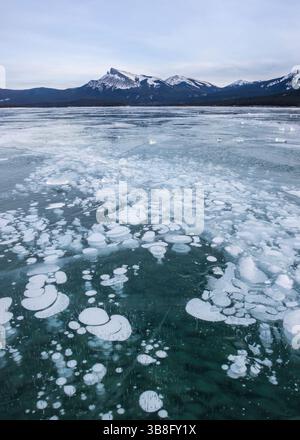 Ein gefrorener See reflektiert die umliegende Bergkette mit einer Vielzahl einzigartiger Eisformationen, die in einem friedlichen Winter über die Oberfläche verstreut sind Stockfoto
