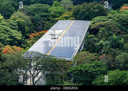 Gebäudedach mit Solarpaneelen Energieeffizienz umgeben von Bäumen. Ökologische Architektur Stockfoto