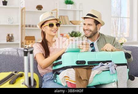 Ein Paar sitzt zu Hause auf dem Sofa und hat den Koffer gepackt, um eine Einkaufsliste für den Urlaub zu machen Stockfoto