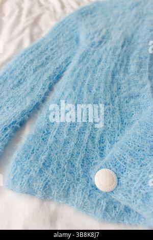 Blaue Strickjacke mit weißem Knopf auf weißem Hintergrund. Weicher blauer Strickpullover mit Details. Hintergrund des Strickmusters. Strickmode für den Sommer Stockfoto