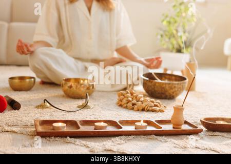 Ruhige Frau, die zu Hause mit Klangschalen, Weihrauch und Kerzen während einer friedlichen Achtsamkeitssitzung meditiert. Stockfoto
