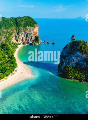 Sonnen Sie sich unter der hellen Sonne am Railay Beach, wo kristallklares Wasser auf weißen Sand trifft, umgeben von dramatischen Kalksteinklippen. Ein idealer Ort für Abenteuerlustige und Erholungssuchende. Stockfoto