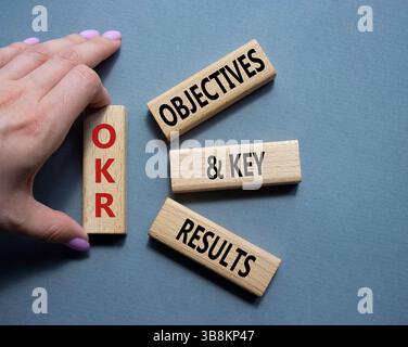 Symbol für OKR-Ziele und wichtige Ergebnisse. Holzblöcke mit den Worten OKR-Ziele und wichtige Ergebnisse. Geschäftsmann Hand. Schöner grauer Hintergrund. Unternehmen Stockfoto