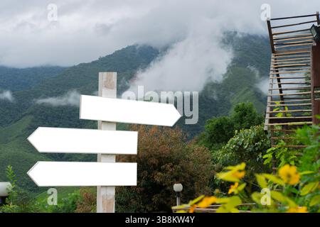 Aufnahme von drei hölzernen Richtungsschildern auf einem Pol über nebeliger Bergkulisse. Kopierraum, Tourismusziel Konzept. Stockfoto