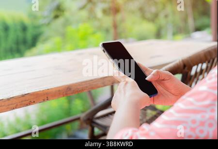 Rückansicht eines nicht erkennbaren jungen weiblichen Touristen, der auf einer Holzbank sitzt und im Urlaub eine Nachricht auf dem Handy liest. Stockfoto