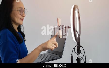 Asiatische Frau mit Laptop, Licht und Smartphone für die Übertragung zu Hause, Lächeln für Benachrichtigung oder Ansage. Online-Konzept. Stockfoto