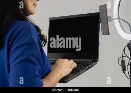 Online-Konzept. Weibliche Influencerin und Vloggerin im Haus mit Laptop, rechtem Licht und mobil, kreative Bewertung für Publikum mit Medientechnologie. Stockfoto