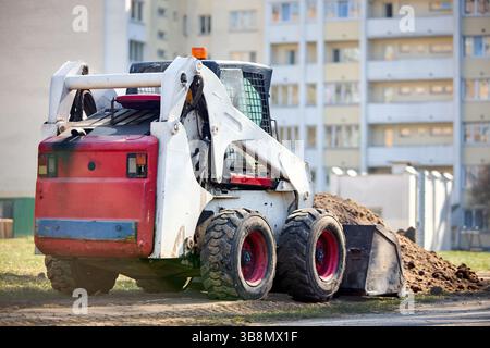 Ein alter schmutziger, rostiger Mini-Planierraupenbagger in der Nähe der Straße über urbanem Hintergrund mit einem selektiven Copyspace-Fokus von drei Vierteln Stockfoto