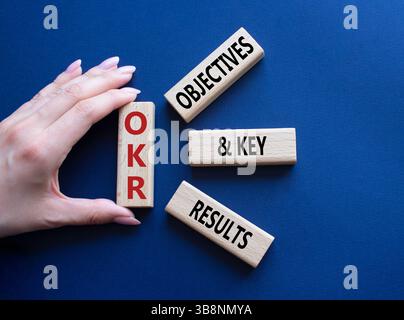 Symbol für OKR-Ziele und wichtige Ergebnisse. Holzblöcke mit den Worten OKR-Ziele und wichtige Ergebnisse. Geschäftsmann Hand. Wunderschöner tiefblauer Hintergrund. Busi Stockfoto