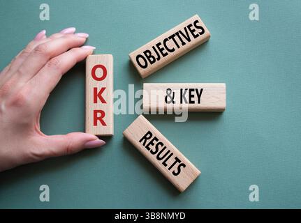 Symbol für OKR-Ziele und wichtige Ergebnisse. Holzblöcke mit den Worten OKR-Ziele und wichtige Ergebnisse. Geschäftsmann Hand. Wunderschöner graugrüner Hintergrund. Bus Stockfoto