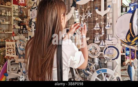 Junge Kundin in einem Souvenirladen für das Meer, die aus einer Vielzahl dekorativer, nautischer Gegenstände in den Regalen des Marktes auswählen Stockfoto