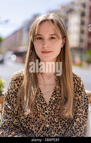 Porträt einer stilvollen jungen Frau mit langen Haaren und einem Hemd mit Leopardenmuster, die einen sonnigen Tag in der Stadt genießt und Selbstvertrauen und modernen Stil ausstrahlt Stockfoto