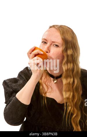 Elegante Frau im dunklen Rüschenkleid küsst sanft die leuchtende orange Hälfte und genießt saftiges und frisches Obst vor weißem Studiohintergrund. Stockfoto