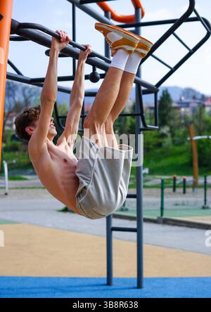 Junger Mann, der an einem sonnigen Tag auf einer Trainingsstation im Park hängende Beinheben durchführt. Stockfoto