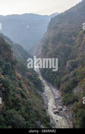 Ein Fluss fließt durch ein steiles, bewaldetes Tal in einer bergigen Region. Das Wasser ist trüb, was auf jüngste Regenfälle hindeutet. Stockfoto