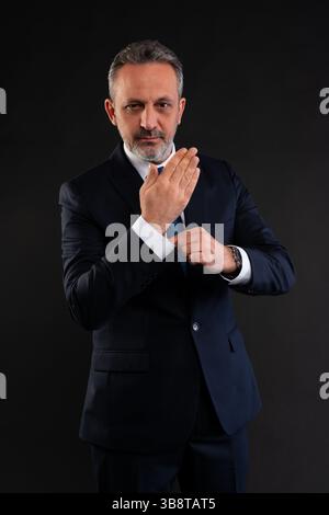 Porträt eines selbstbewussten, Reifen Geschäftsmannes, der seine Hemdmanschette anpasst, während er in die Kamera blickt. Stilvoll und professionell. Stockfoto