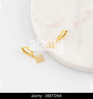 Elegante goldene Starburst-Ohrringe mit Diamanten auf Marmoroberfläche. Schmuck Stockfoto