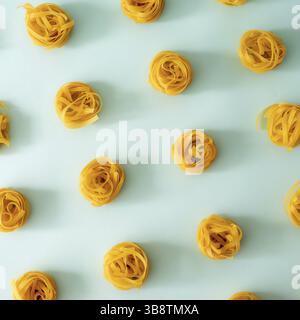 Pasta Art Muster. Tagliatelle auf blauem Pastellhintergrund. Kreatives Layout mit Nudelnudeln, Draufsicht oder flach liegend. Quadratische Freistellung. Kreatives Design für m Stockfoto