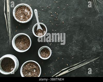 Leinsamen und trockenes Roggenohr auf dunklem Hintergrund. Set aus kleinen Schüsseln mit Bio-Flachssamen oder Leinensamen. Leinsamen sind reich an Omega-3-Fettsäuren. Kopieren Stockfoto