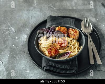 Zucchini Parmesan Fleischbällchen mit Pasta Carbonara in schwarzem Craft Teller auf grauem Hintergrund. Nahaufnahme von cremigem Carbonara mit Kopierraum links Stockfoto