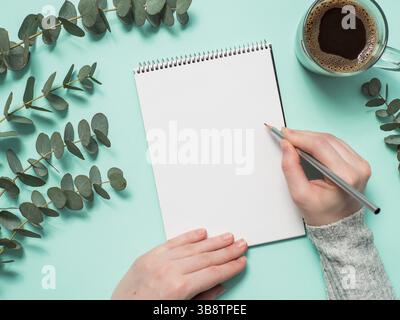 Leeres Papier Notebook und weibliche Hände mit Bleistift. Leere Papier Skizzenbuch mit pincil in Frau Hände auf blauem Hintergrund. Top View oder flach. Kopieren Sie sp Stockfoto