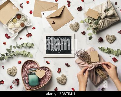 Valentinstag-Konzept ohne Verschwendung. Umweltfreundliche Geschenktuchverpackung im Furoshiki-Stil, hausgemachte Süßigkeiten und Kerze als Geschenkideen und Kreidetafel mit Stockfoto