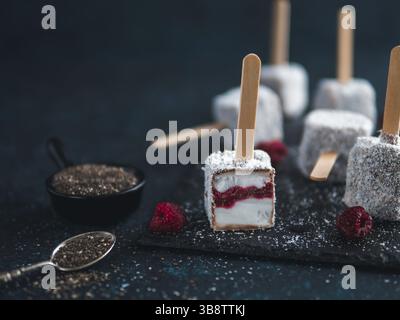 Hausgemachte raw lamington Eis erscheint auf dunklem Hintergrund. Australische süße Nachspeise lamington mit Chia und Himbeeren Marmelade, Schokolade und Kakao. Stockfoto