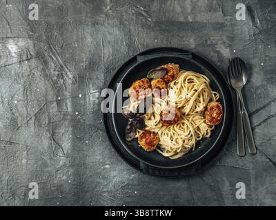 Zucchini Parmesan Fleischbällchen mit Pasta Carbonara in schwarzer Bastelplatte auf grauem Hintergrund. Nahaufnahme von cremiger Carbonara mit Kopierraum. Bis Stockfoto