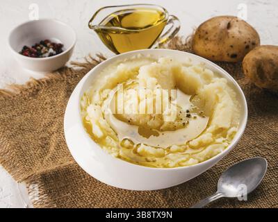 Kartoffelpüree in Weiß Schüssel mit Sack, Pfeffer und Olivenöl auf strukturierte konkrete weißer Hintergrund Stockfoto