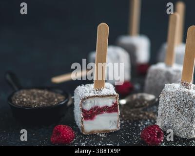 Hausgemachte raw lamington Eis erscheint auf dunklem Hintergrund. Australische süße Nachspeise lamington mit Chia und Himbeeren Marmelade, Schokolade und Kakao. Stockfoto