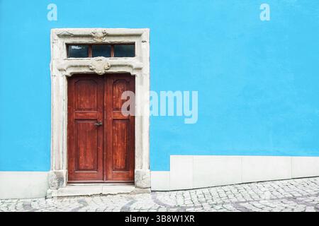 Alte Holztür Eingang. Hellblauer Wandhintergrund. Historisches Architekturelement. Rustikaler Vintage-Eingang. Europäisches Straßendetail. Urbanes Äußere. Stockfoto
