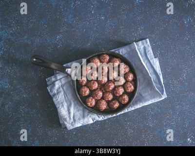 Hausgemachte Fleischbällchen aus gebratenem Rindfleisch in gusseiserner Pfanne auf dunkelblauem Hintergrund. Draufsicht oder flach. Kopierbereich für Text Stockfoto