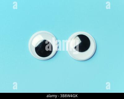 Schöne Augen auf blauem Hintergrund. Draufsicht oder flach liegend. Kunststoff Spielzeug Augen auf türkisfarbenem Hintergrund Stockfoto
