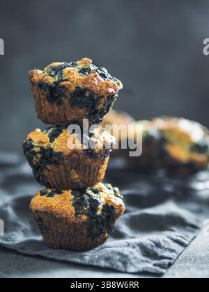 Hausgemachte vegane Heidelbeermuffins auf dunklem Hintergrund. Stapel mit drei eierfreien Muffins mit Kopierraum für Text oder Design. Low-Taste. Vertikal Stockfoto
