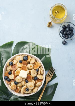 Trendiges Essen - Pfannkuchen-Müsli. Haufen Mini-Müslipfannkuchen in boul auf blauem Hintergrund. Platz für Text kopieren. Draufsicht oder flache Lagen. Vertikal Stockfoto