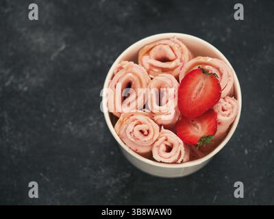 Gerolltes Eis mit Erdbeere in Kegelbecher auf dunklem Hintergrund. Erdbeer Eisrollen Draufsicht oder flach legen. Thailändisches Eiscreme mit Copy Spa Stockfoto