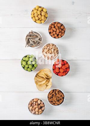 Auswahl an verschiedenen Snacks für Bier, Wein, Party. Erdnüsse in Kokosglasur, grüne Vasabi, rote scharfe Chili, Gelbkäse und Chips, Pistazien Stockfoto