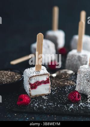 Hausgemachte raw lamington Eis erscheint auf dunklem Hintergrund. Australische süße Nachspeise lamington mit Chia und Himbeeren Marmelade, Schokolade und Kakao. Stockfoto