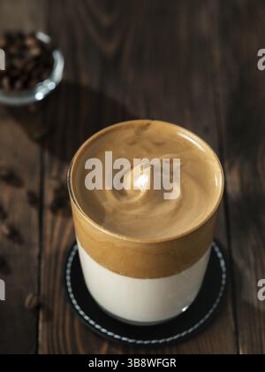 Trendiges koreanisches Getränk - Dalgona Kaffee. Glas mit kaltem oder heißem Getränk - Schlagkaffee mit Milch und Kaffeebohnen auf braunem Holzbackgrou Stockfoto