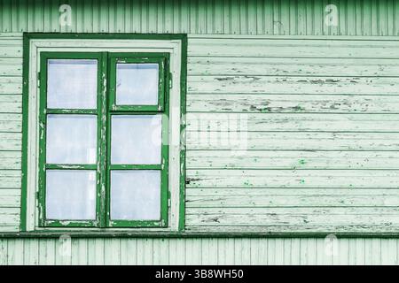 Alte grüne Holzwand. Einzelfenster mit weißem Glas. Rustikales Hausdesign. Hintergrund verwitterter Dielen. Traditionelle ländliche Architektur. Stockfoto